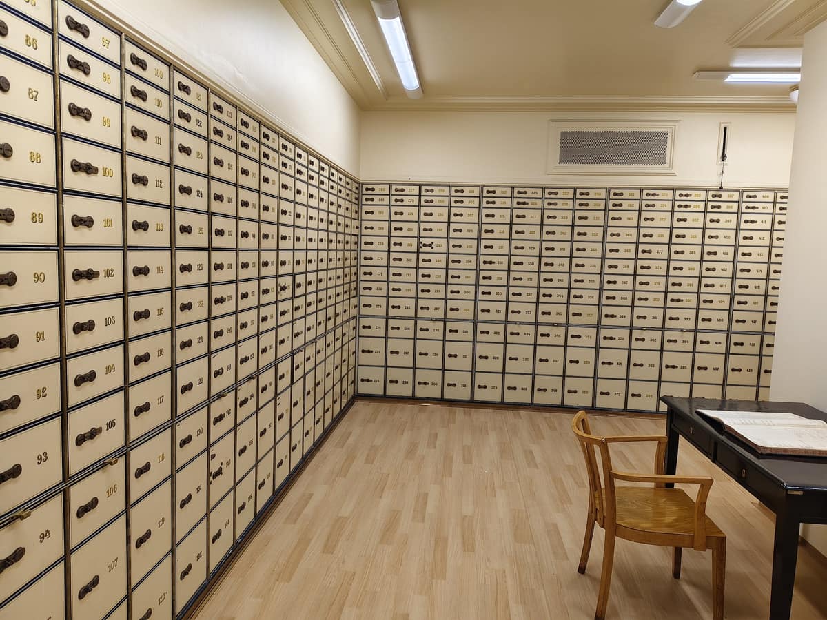 A secure safe-deposit room with walls of numbered, locked metal boxes, a wooden chair and a table.