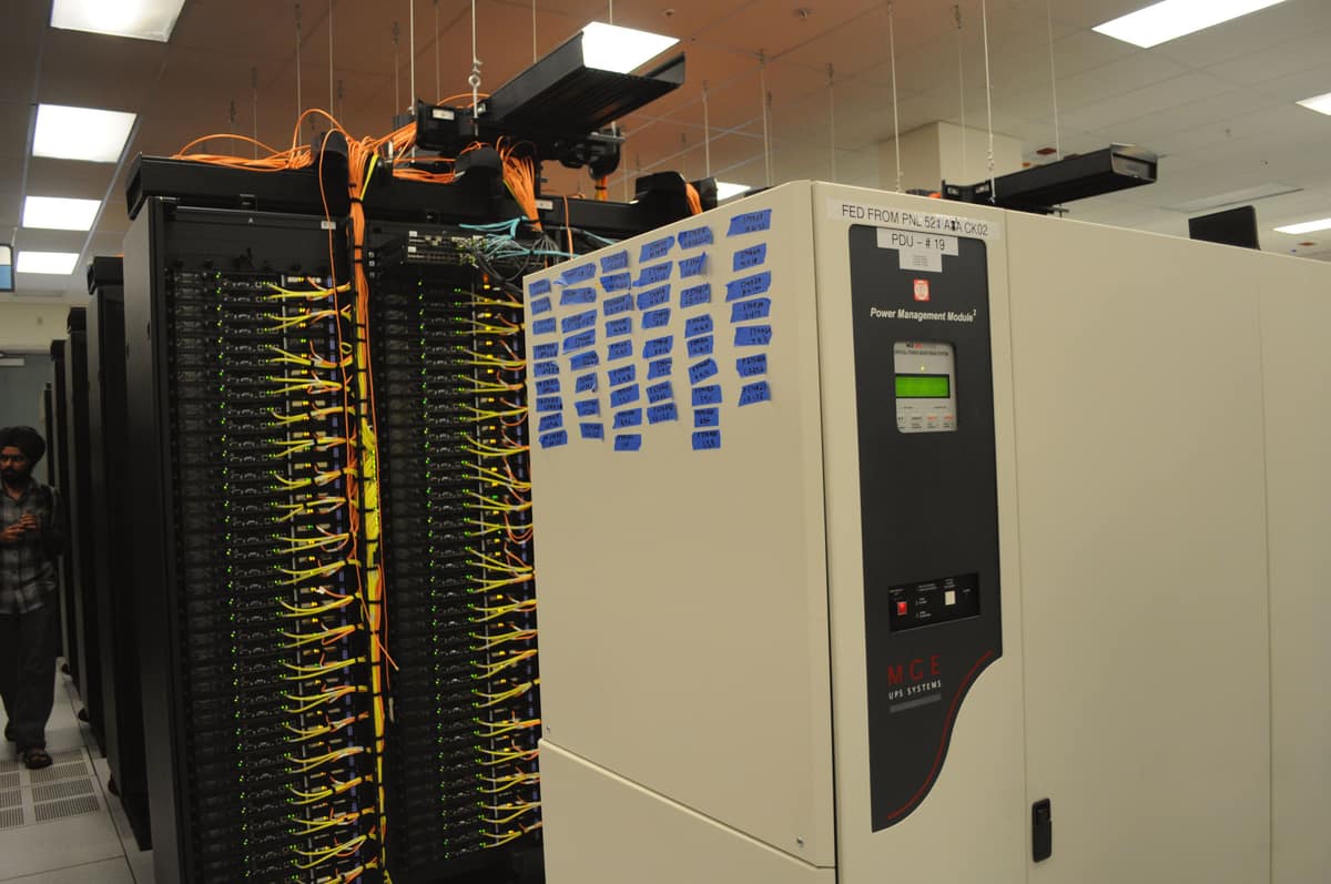 Racks with dense network cabling beside a floor-standing UPS power management module in a data centre