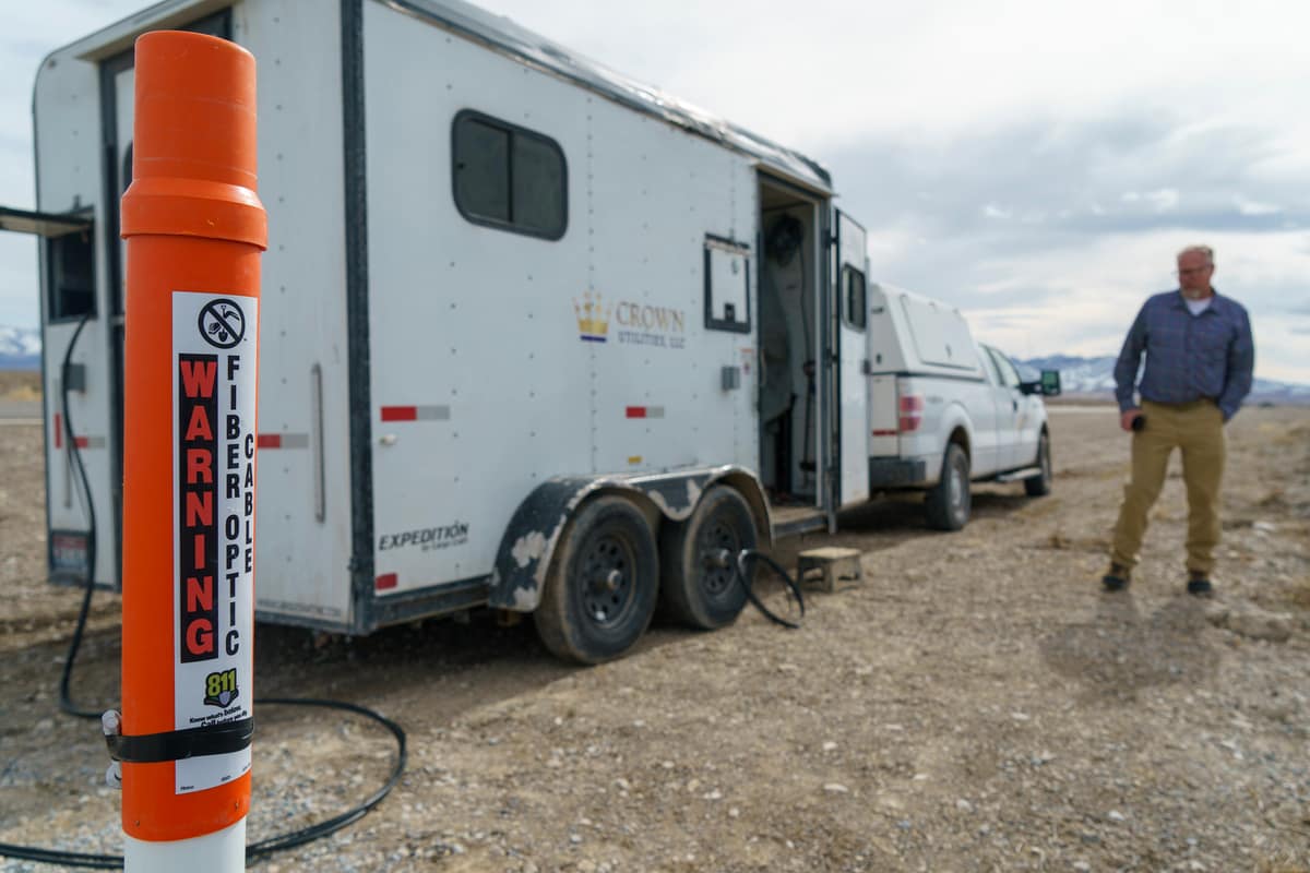Fibre installation trailer and truck at an outdoor site, with a buried-fibre warning marker in the foreground