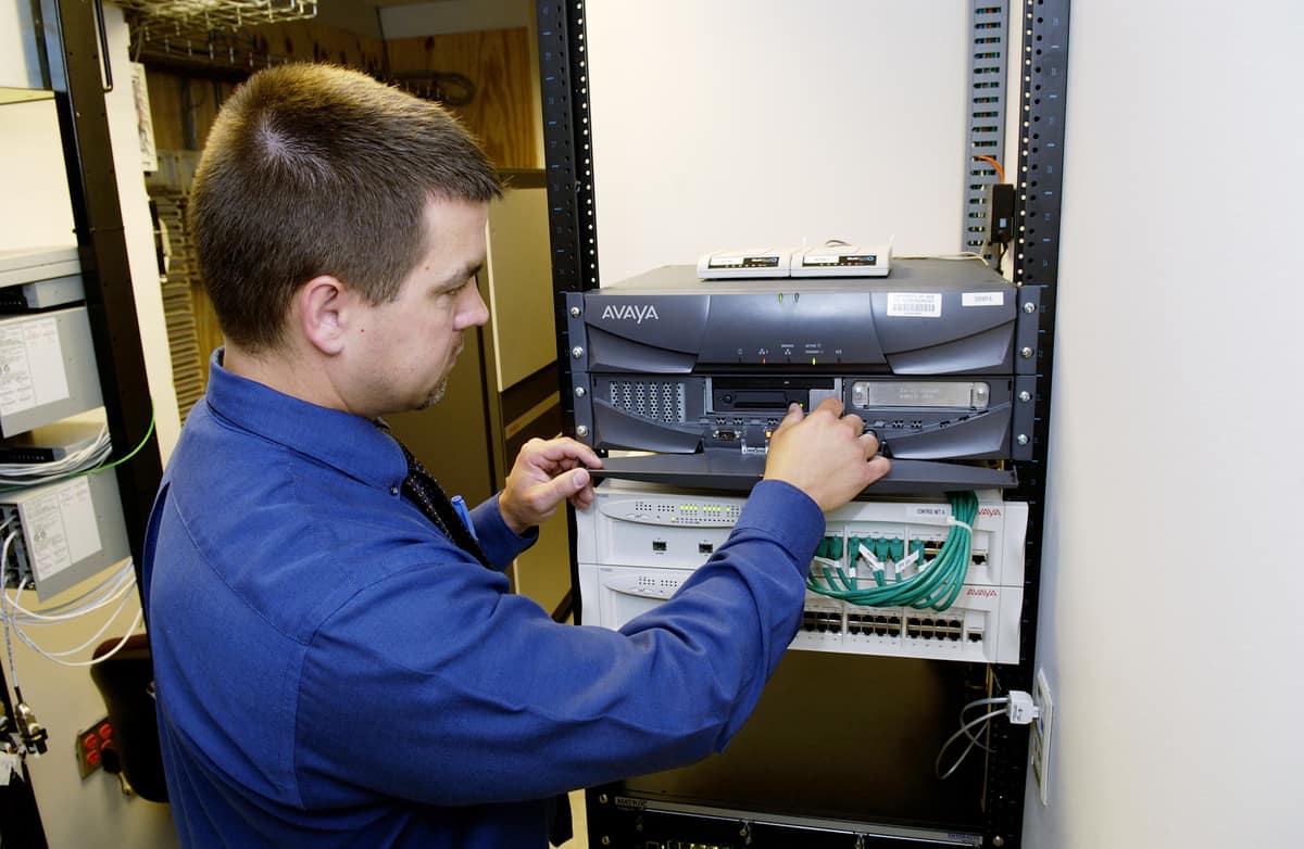 Technician working at the front of a wall-mounted network rack with a switch and patched cabling